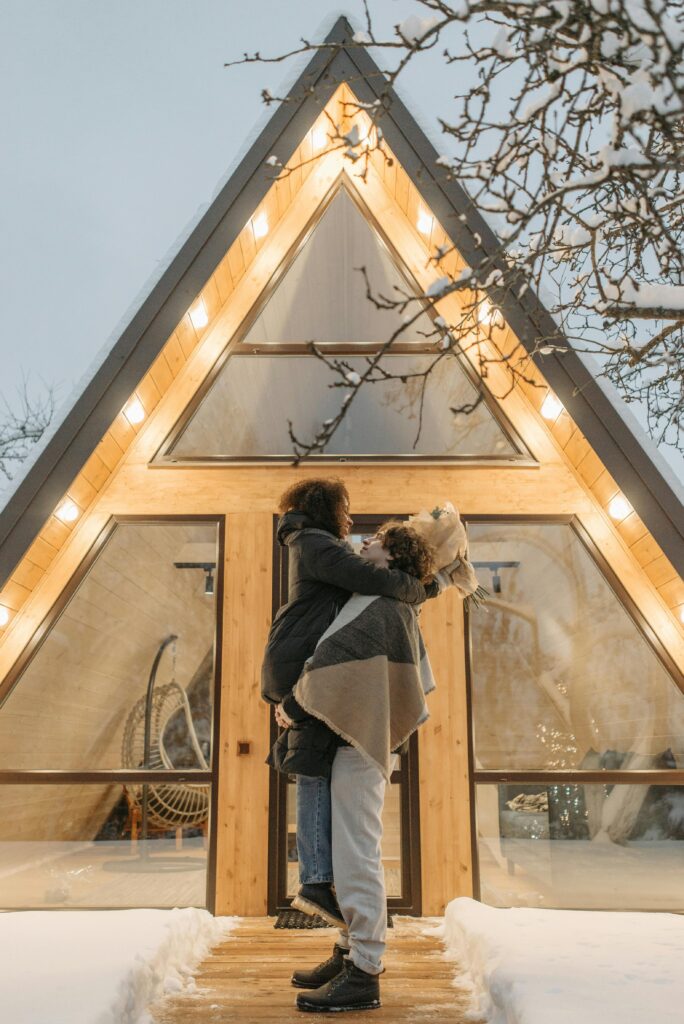 pexels-photo-6550035-6550035 Loving couple embracing in front of a cozy A-frame cabin during winter.